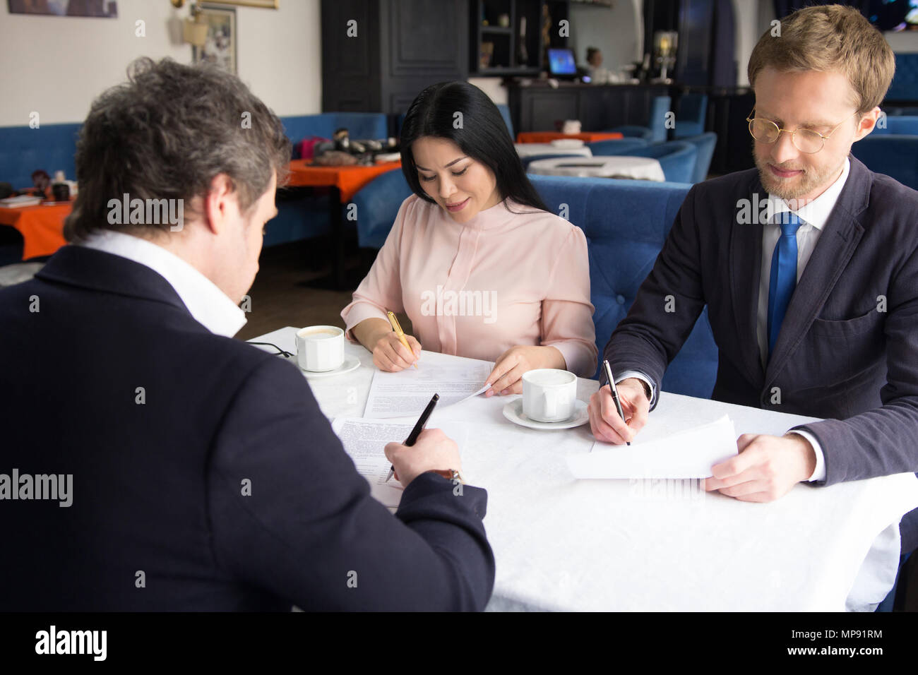 Tre uomini di affari che firmano un accordo presso il ristorante Foto Stock