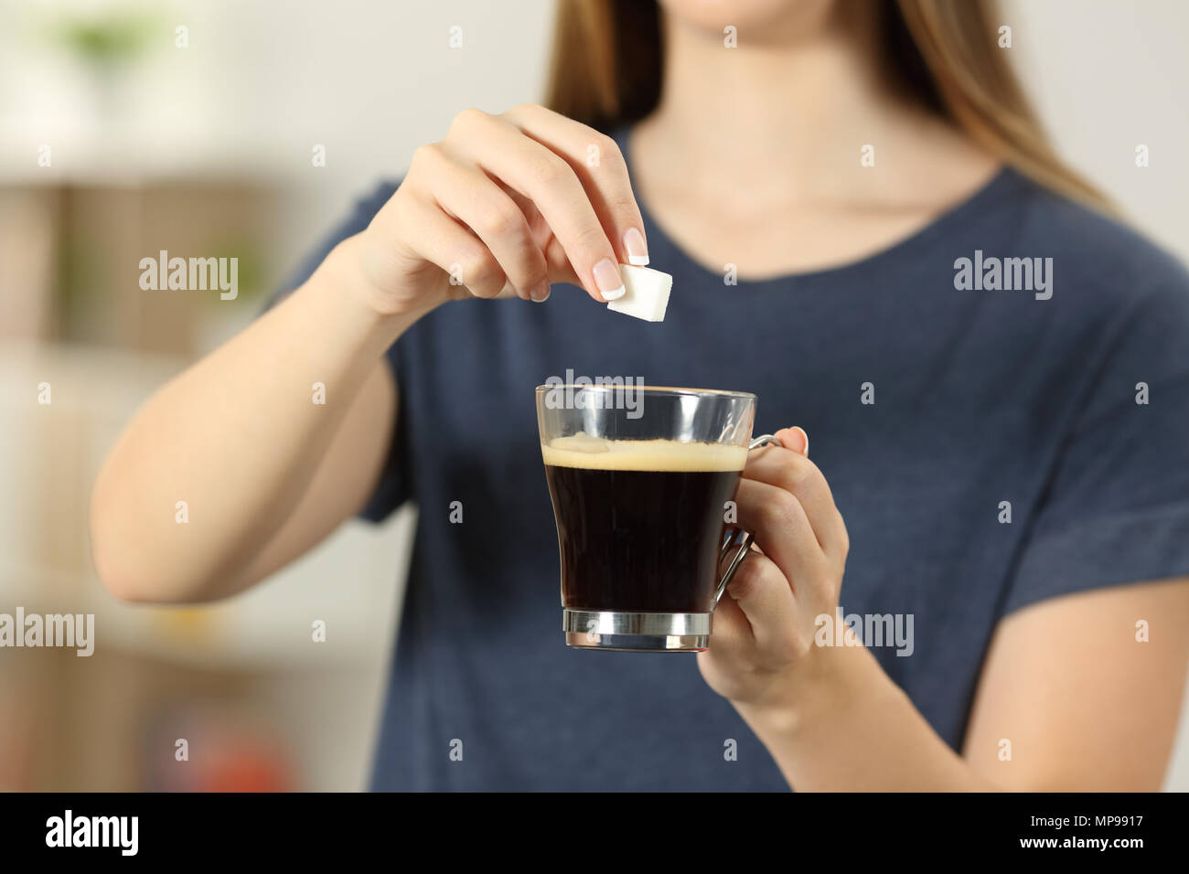 Vista frontale in prossimità di una donna mani di gettare una zolletta di zucchero in una tazza di caffè a casa Foto Stock