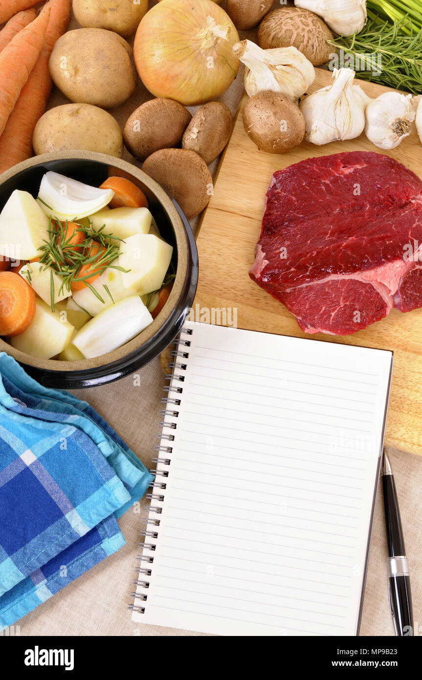 Preparazione della carne di manzo casseruola o stufato con ingredienti ed erbe su cucina tagliere e fustellato ricettario. Foto Stock