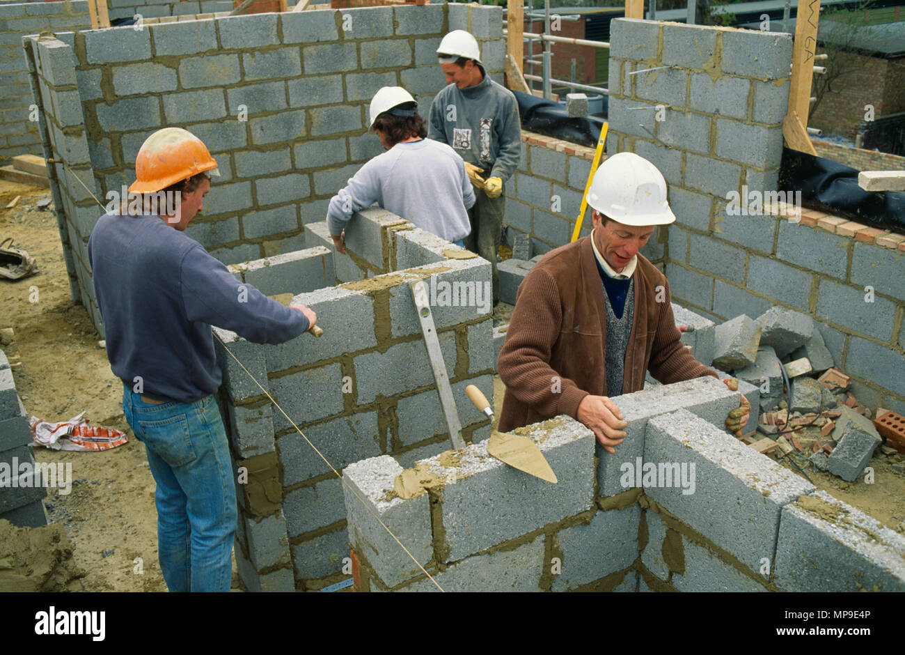 Architettura, Edilizia, uomini al lavoro sul sito di costruzione Indossare copricapi rigidi che stabilisce i corsi di blocchi in calcestruzzo. Foto Stock
