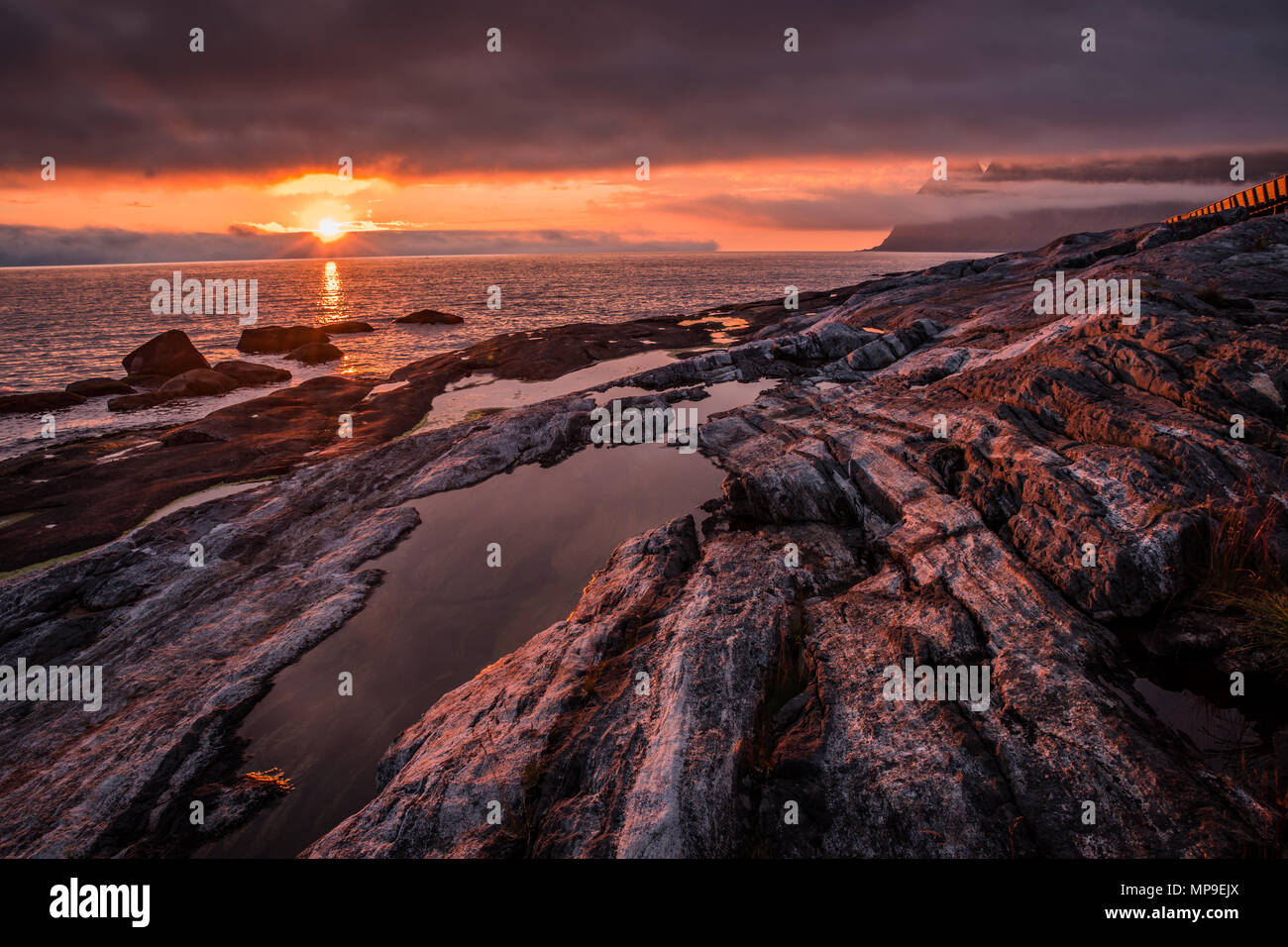 Drammatico, rosso e arancione estate fiery tramonto sulla spiaggia rocciosa con pozzanghere d'acqua. Prese su isola di Senja, Norvegia. Foto Stock