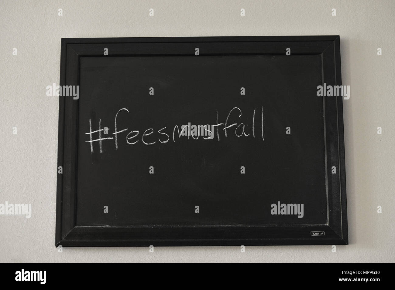 #Feesmustfall scritto in bianco gesso su una parete montata Blackboard. Foto Stock