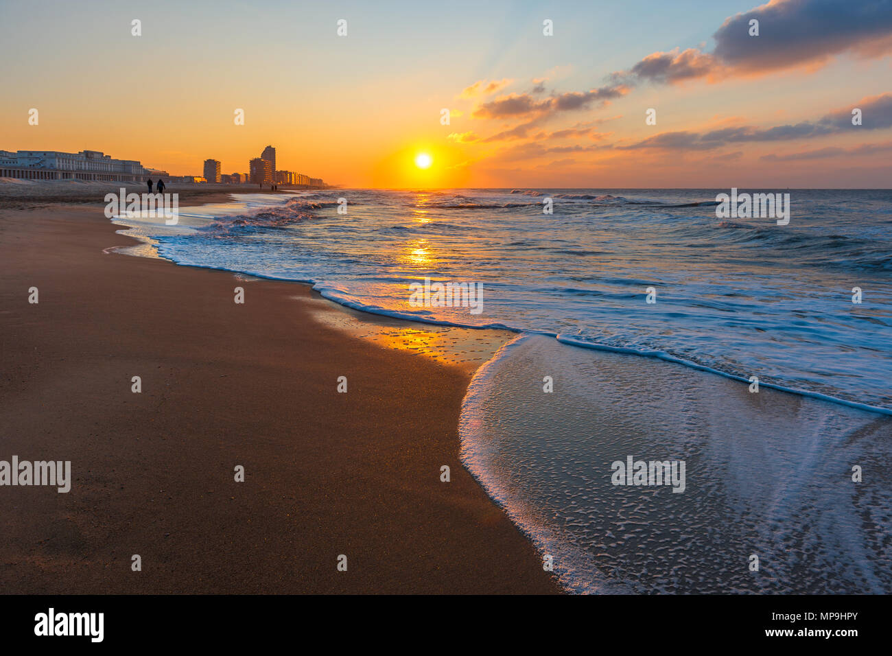 Tramonto lungo la spiaggia del Mare del Nord di Ostenda in città con il suo skyline urbano e la silhouette di una coppia avente una passeggiata, Fiandre Occidentali, Belgio. Foto Stock