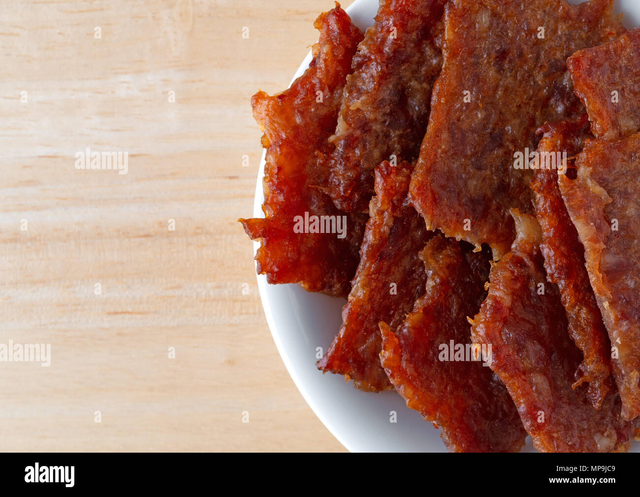 Top vista ravvicinata di una piccola ciotola bianco riempito con carne di maiale marinato a scatti su una tavola di legno. Foto Stock