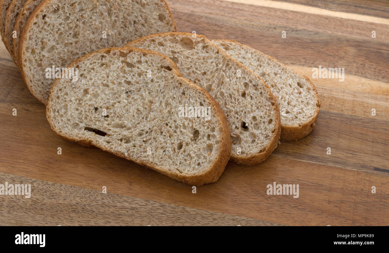 Vista ravvicinata di fette di pane di grano di fronte a una piccola focaccia su un legno tagliere. Foto Stock