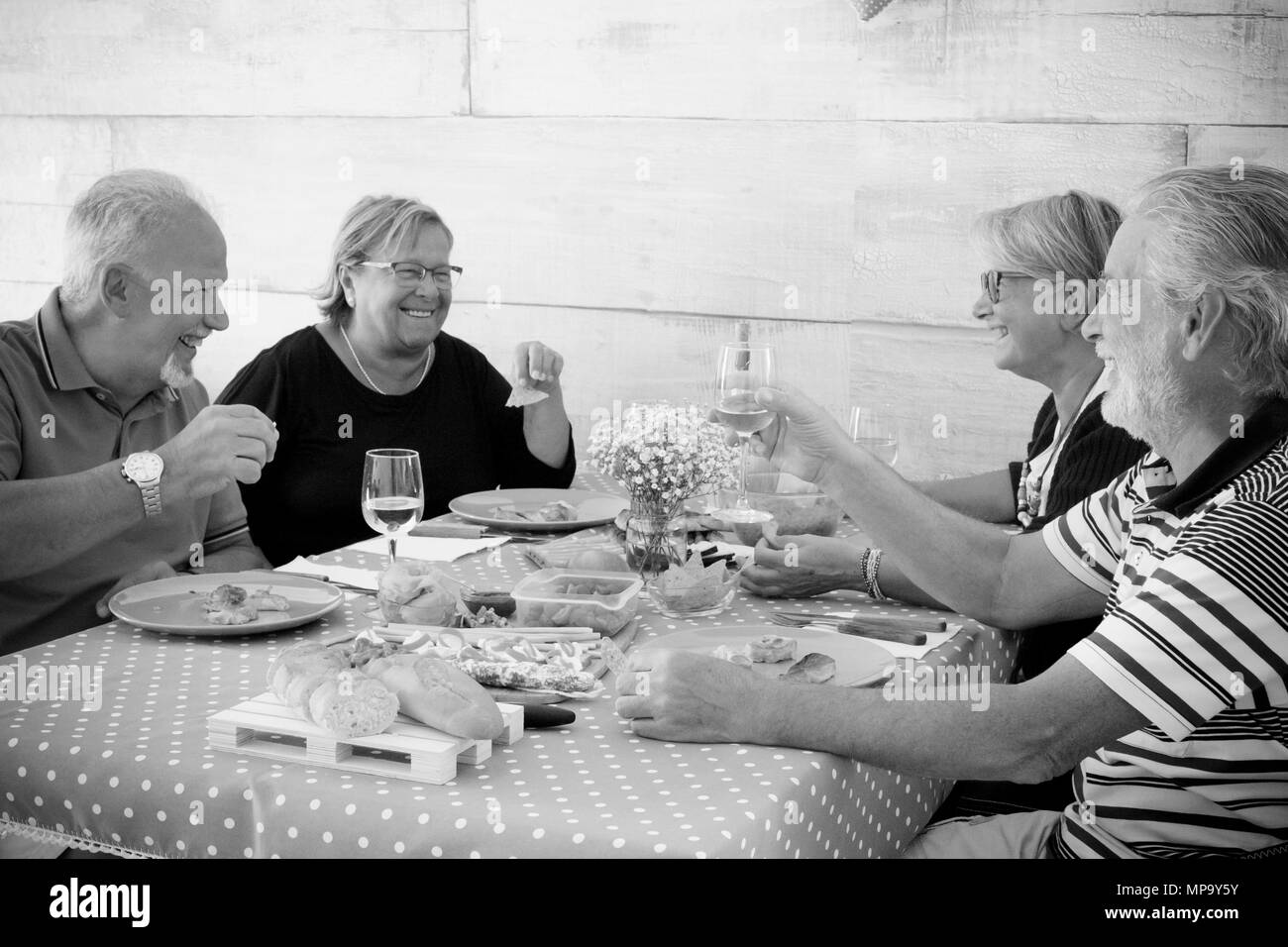 Home scena per un gruppo di anziani in bianco e nero. Mangiare e ridere insieme con bicchieri di vino e cibo. bel tempo con persone e cose gustosi o Foto Stock
