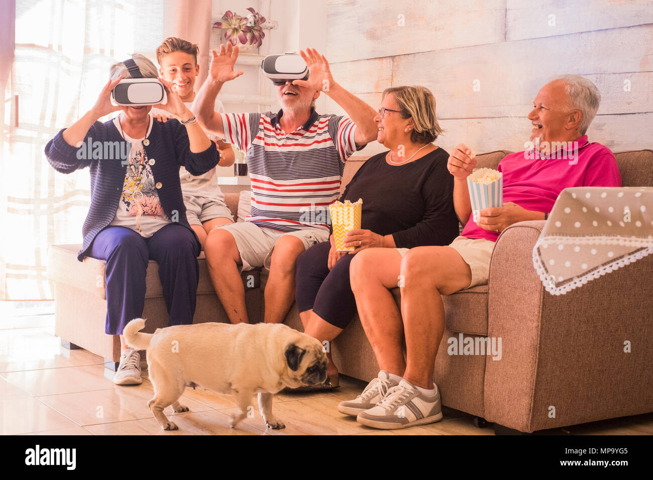 Gruppo di persone mescolati a generazione da senior di adolescente divertirsi a casa cercando la moderna tecnologia goggled auricolare sul divano. ridere e sorridere e Foto Stock