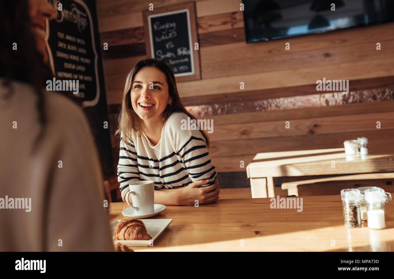 Donna sorridente seduto in un ristorante a parlare con il suo amico. Amici seduti in un caffè con caffè e snack sulla tabella. Foto Stock