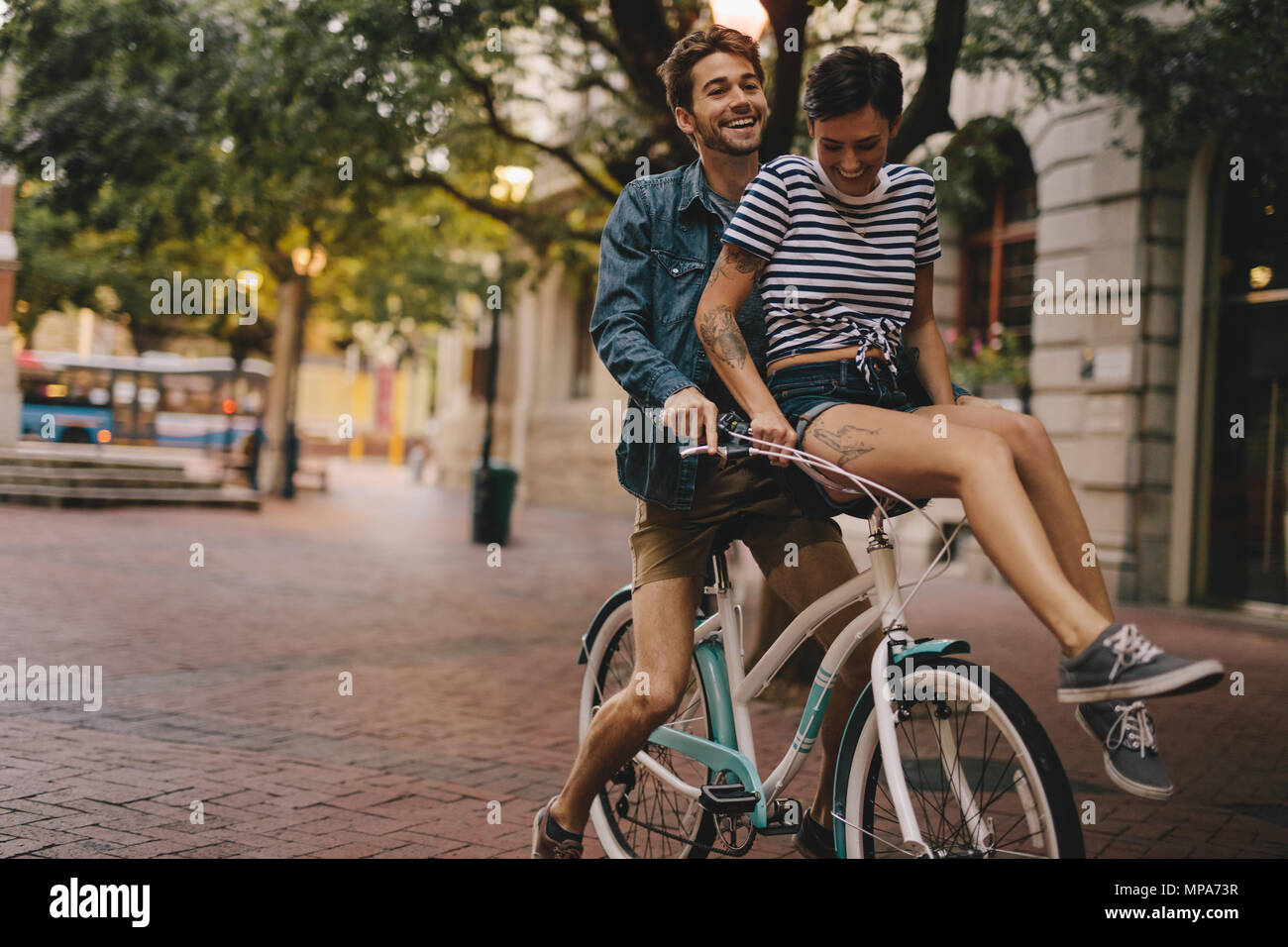Giovane uomo e donna in sella ad una bicicletta in città. Coppia felice su una bicicletta in città. Foto Stock