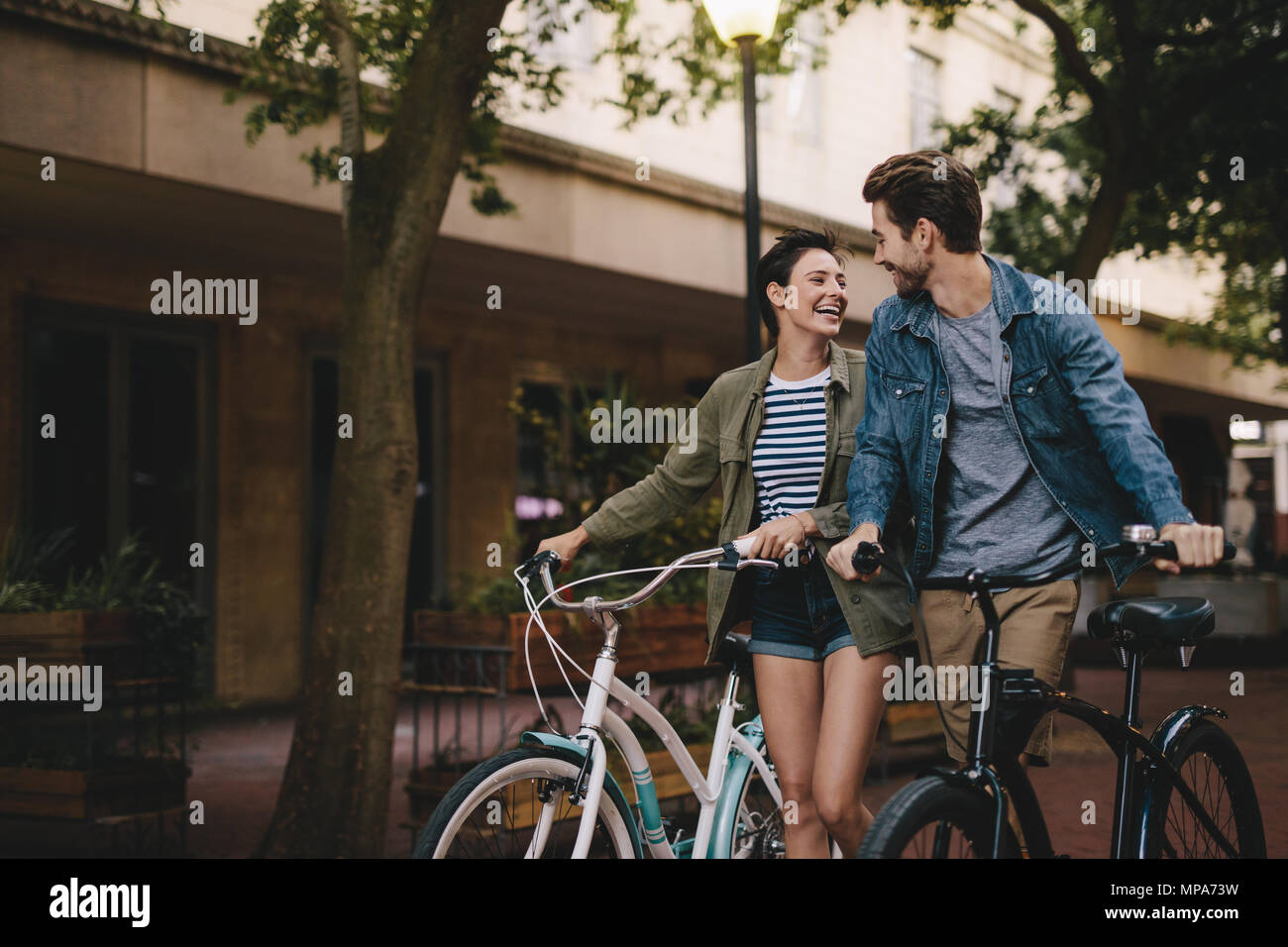 Felice l'uomo e la donna a camminare su una strada con le loro biciclette. Coppia giovane con le biciclette sulla strada della citta'. Foto Stock