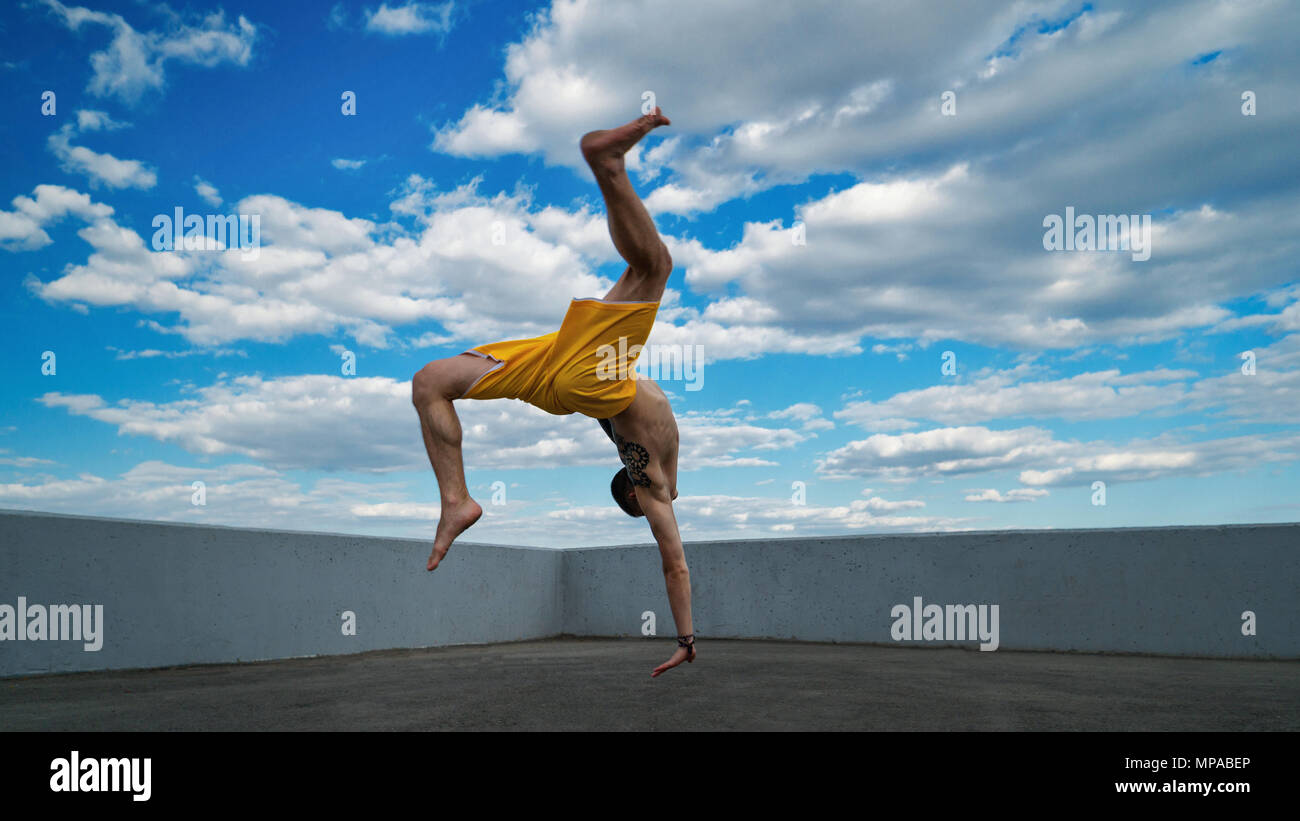 Ingannare sulla strada. Arti marziali. L'uomo fa back flip con supporto per il braccio a piedi nudi. Ripresi dal fondo scorcio contro sky. Foto Stock