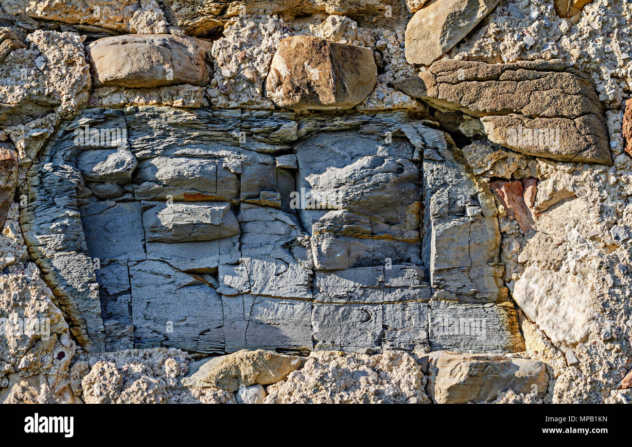 Pezzo grosso di ardesia incrinato in un antico muro di pietra. La costruzione in muratura. Parete ruvida, fatta di campo allentato le pietre e la malta senza intonaco. Foto Stock