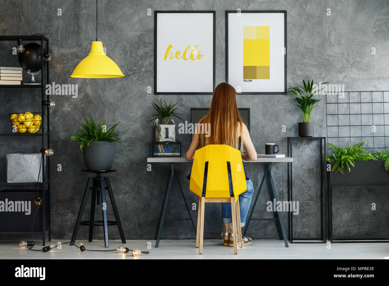 Ragazza seduta alla sua scrivania in poster mock-up interno con studio di spazio e moderna sedia giallo Foto Stock