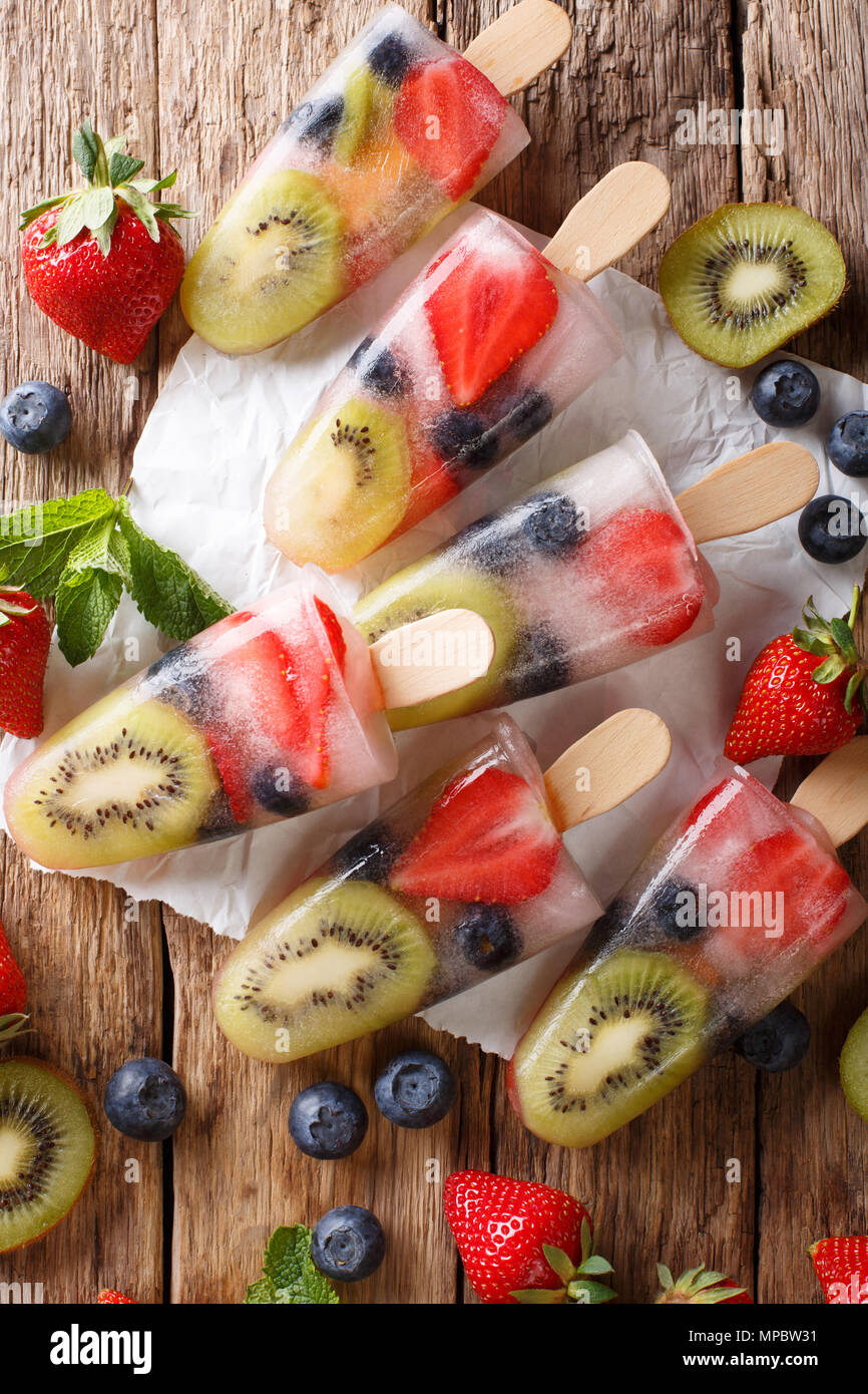 Bacca naturale di frutta da ghiaccio con fragole fresche, mirtilli e kiwi vicino sul tavolo. Verticale in alto vista da sopra Foto Stock