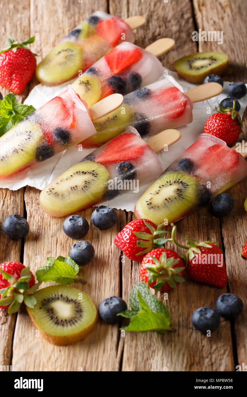 Una sana frutta intera Popsicles con bacche Fragole Kiwi closeup su legno tabella vintage verticale. Foto Stock