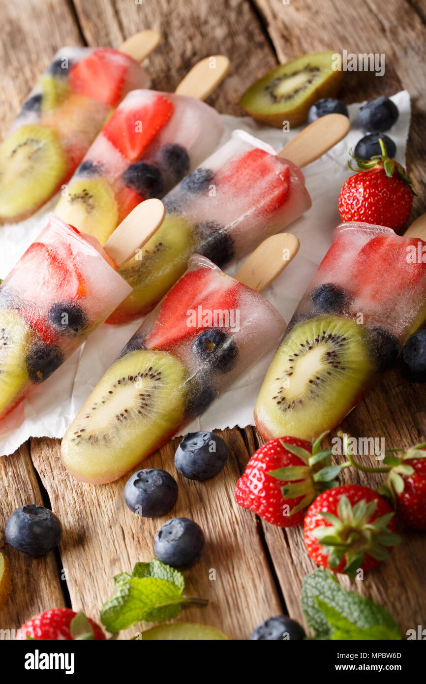 Preparate di fresco popsicles ghiaccio con fragole fresche, kiwi e mirtilli su un bastone di close-up su una tavola verticale. Foto Stock