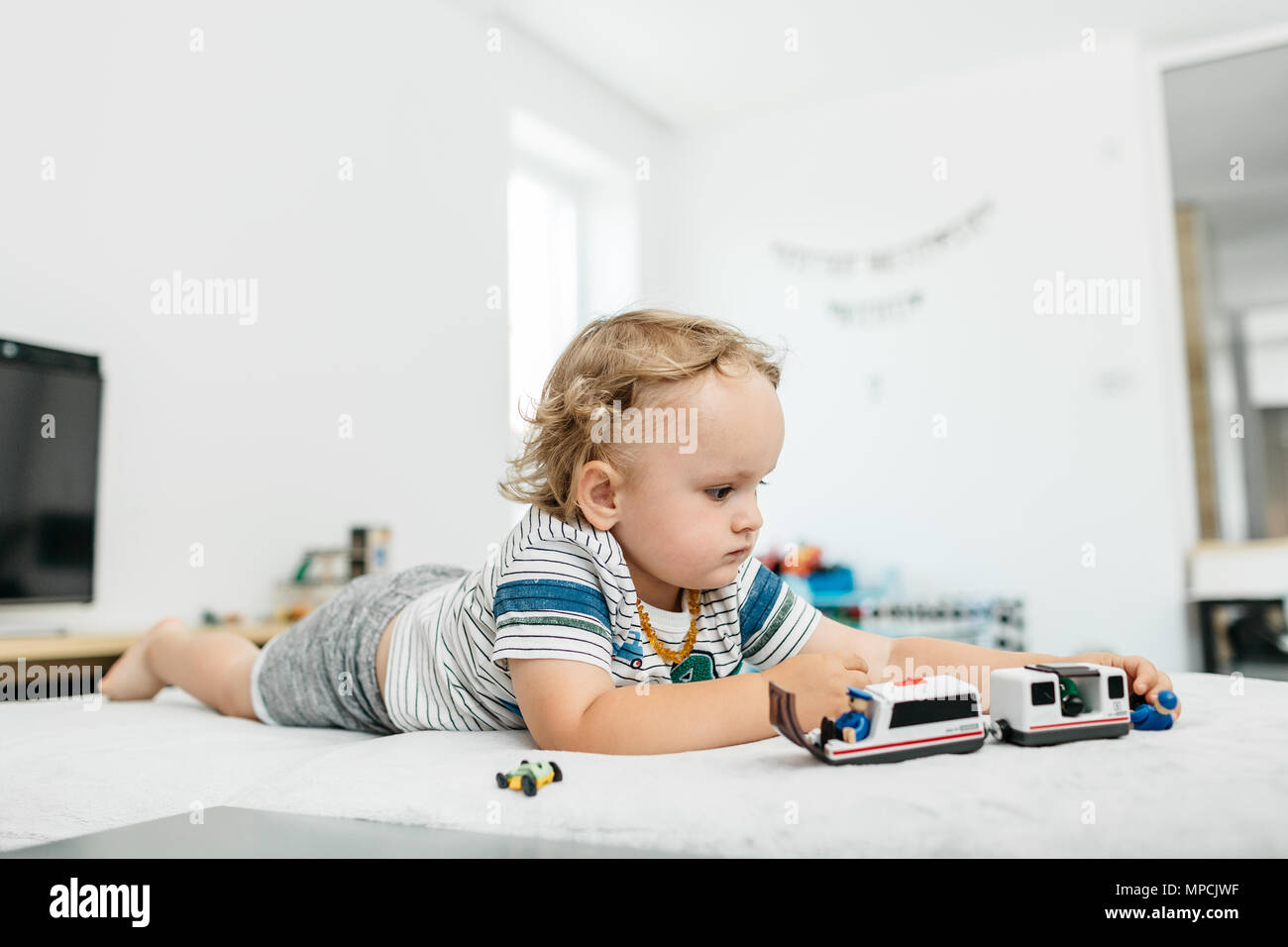 Un giovane ragazzo giocando con i giocattoli sul suo proprio a casa. Un bimbo che gioca da se stesso con i veicoli di legno. Foto Stock