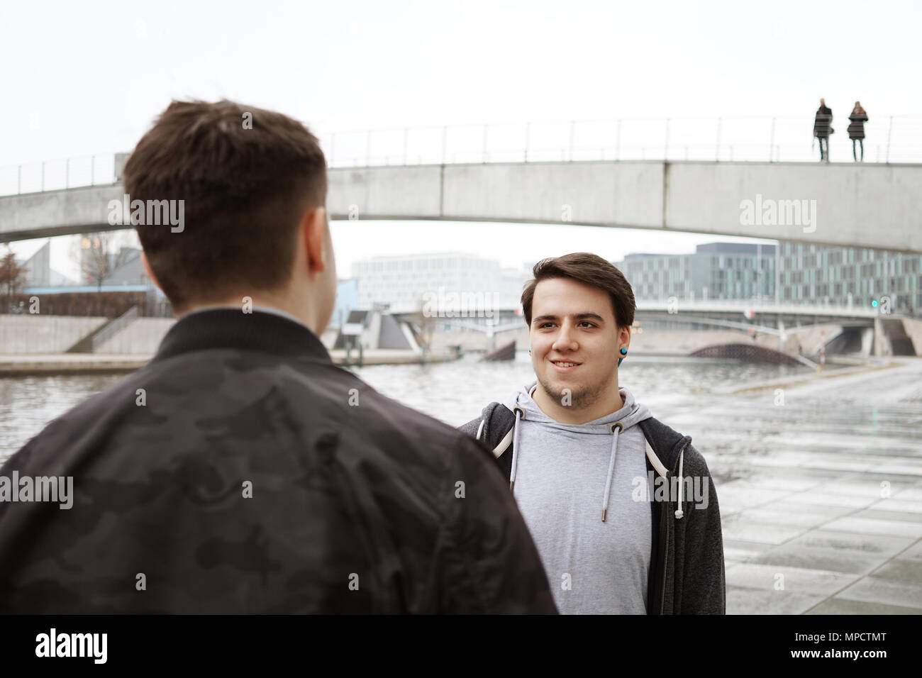 Due adolescenti maschi amici avente una conversazione, stile di vita o la vita della città di concetto, urban posizione sulla riva del fiume a Berlino Germania Foto Stock