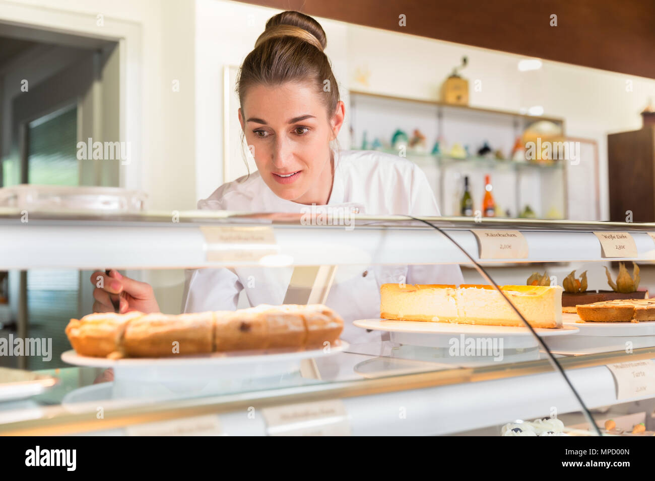 Donna di vendite nel negozio di pasticceria torte mettendo sul display Foto Stock Donna di vendite nel negozio di pasticceria torte mettendo sul display Foto Stock