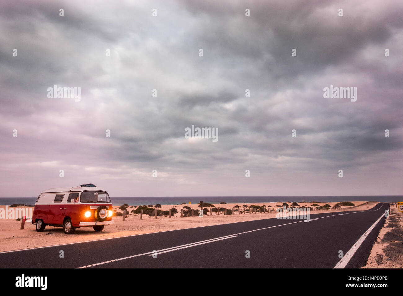 Red vecchio van con luci su parcheggiata vicino all'oceano. Lungo la strada attraverso il deserto di Fuerteventura Corralejo. Foto Stock