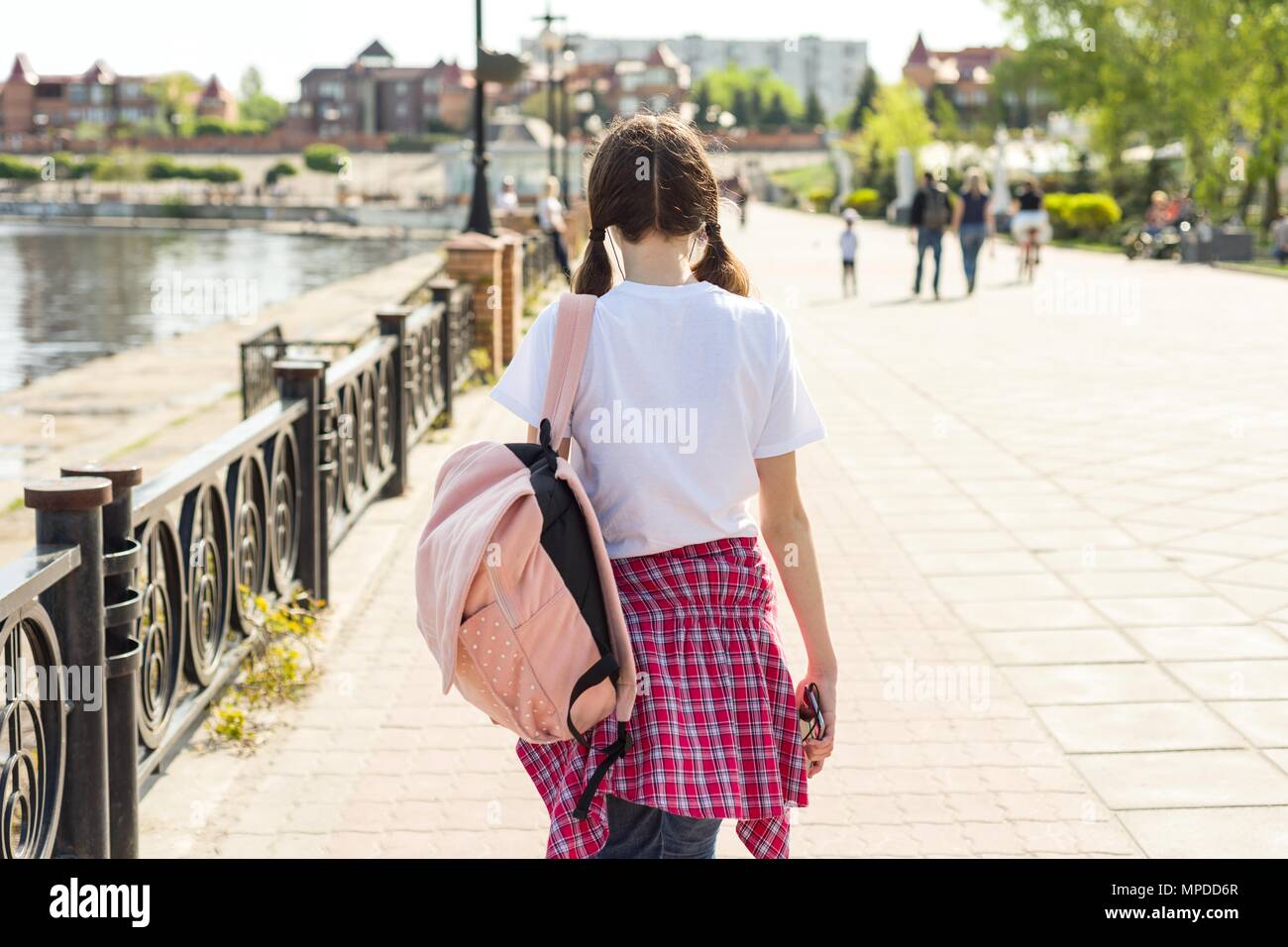 Studente adolescente ragazza camminare per la strada con lo zaino. Si torna a scuola, vista posteriore. Foto Stock