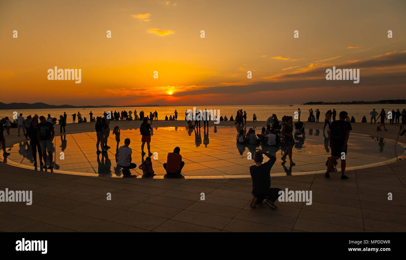 Villeggianti e turisti ammirano una gloriosa arancione tramonto dal photovolt installazione, il monumento al sole nel porto di Zadar croazia Foto Stock