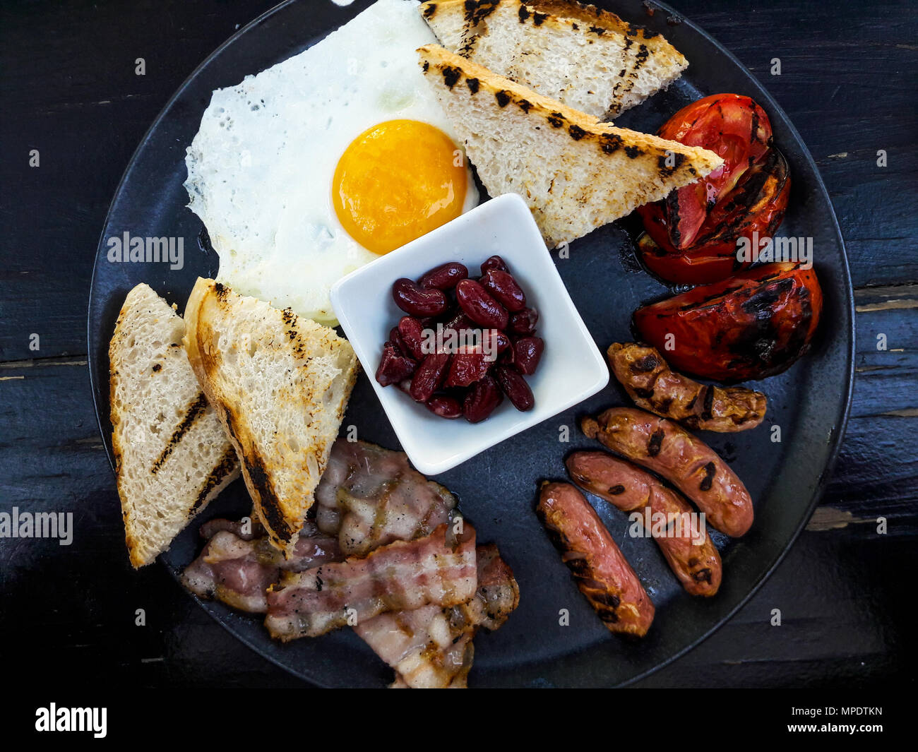Prima colazione Inglese con pancetta, fagioli rossi, salsiccia, uova fritte e pane sulla superficie nera. Foto Stock