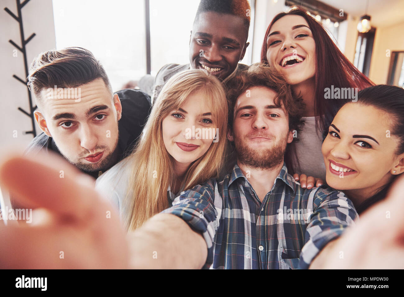 Amici divertendosi al ristorante.due ragazzi e 4 ragazze bere rendendo selfie, facendo segno di pace e di ridere. Sul primo piano donna azienda smart phone. Tutti indossare abiti casual Foto Stock