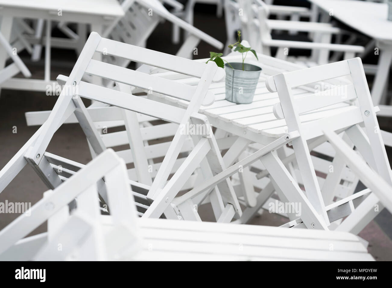 Cumuli di invertiti sedie in plastica bianca su tavoli nel ristorante chiuso sulla terrazza di close-up. Bella grafica, caos interessante sullo sfondo Foto Stock