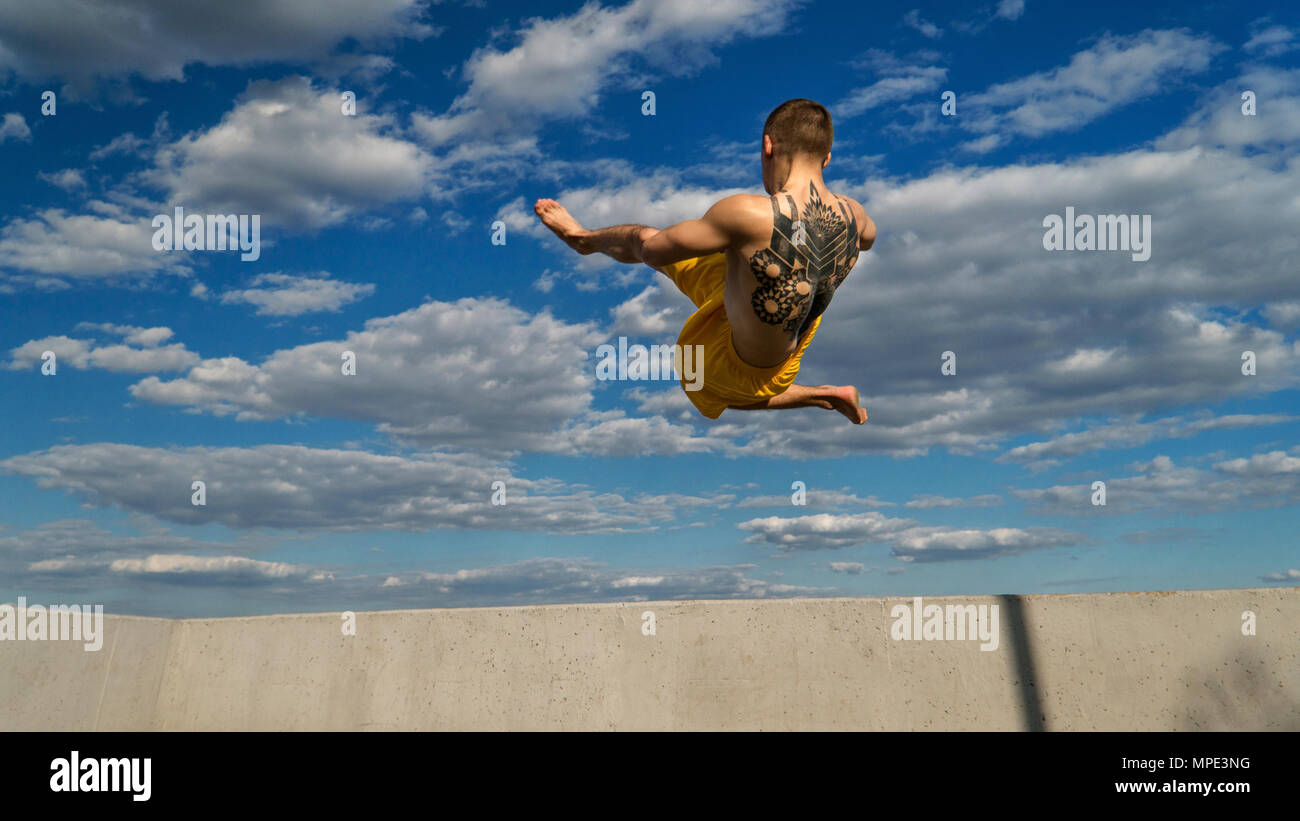 Ingannare sulla strada. Arti marziali. L'uomo fa salto in alto a piedi nudi. Ripresi dal fondo scorcio contro sky. Foto Stock
