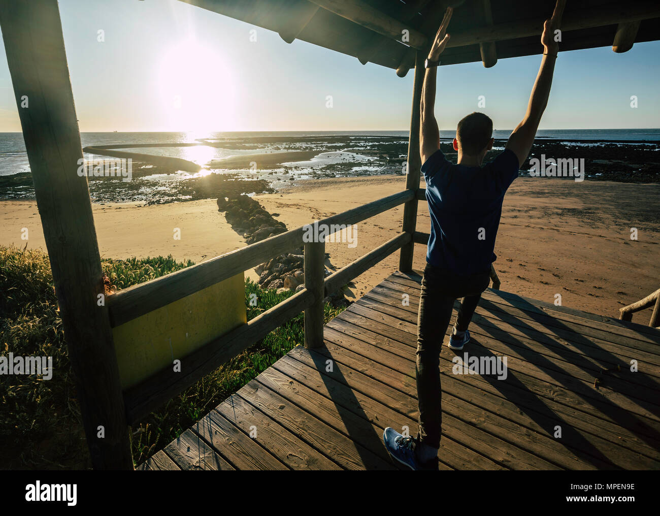 Giovane uomo a praticare yoga al molo con la spiaggia di Sanlúcar di Barrameda in background, in un bel tramonto Foto Stock
