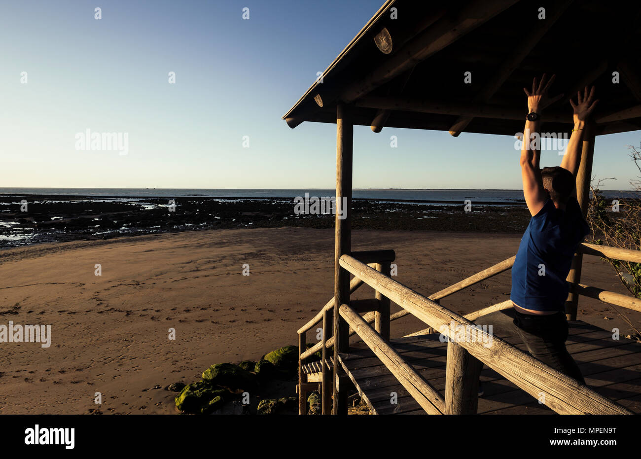 Giovane uomo a praticare yoga sul molo con Sanlucar de Barrameda spiaggia in background Foto Stock
