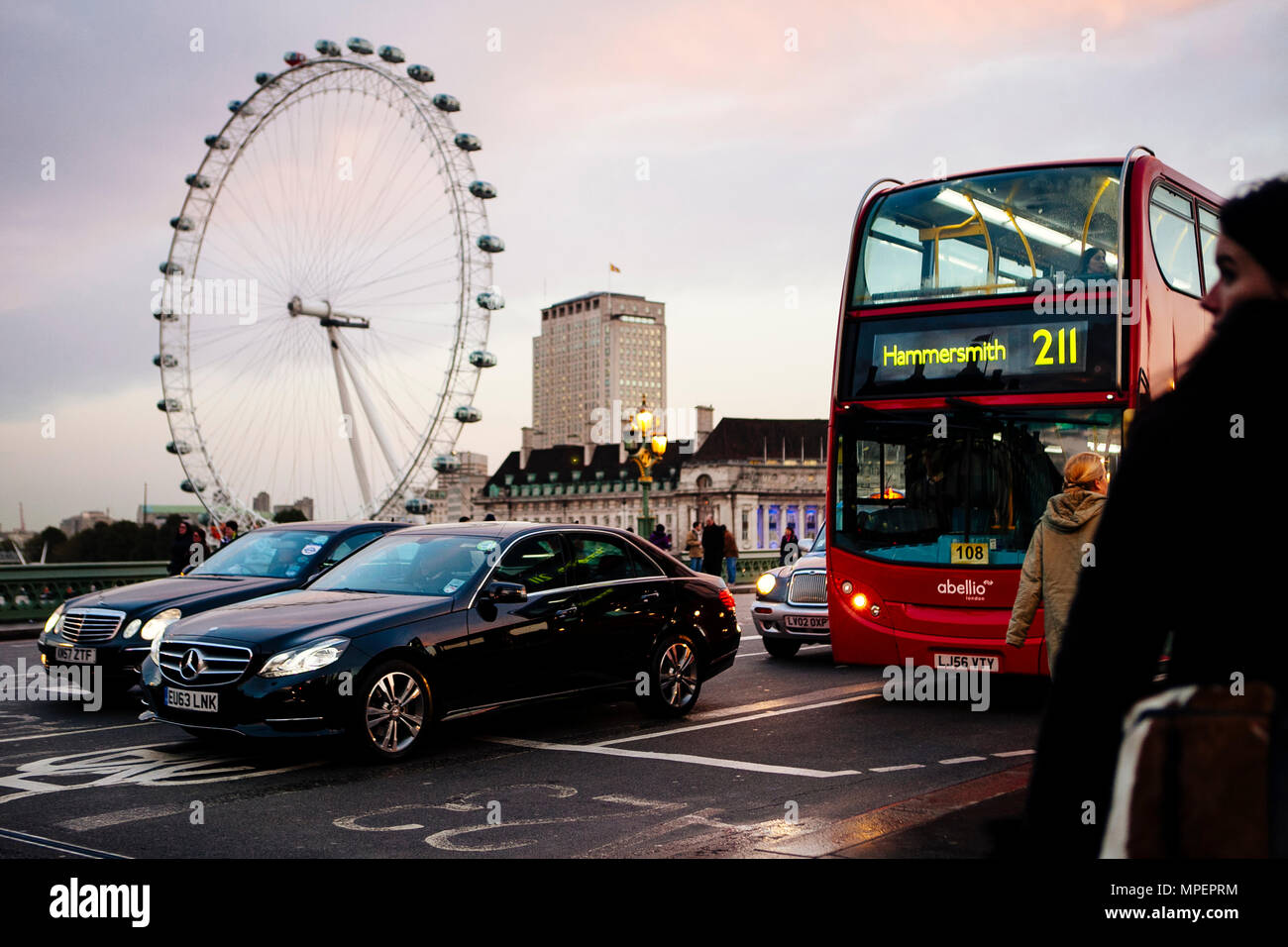 La gente in attesa per il traffico sul Westminster Bridge oltre il Tamigi con la London Eye o Millennium Wheel in prima serata. Foto Stock