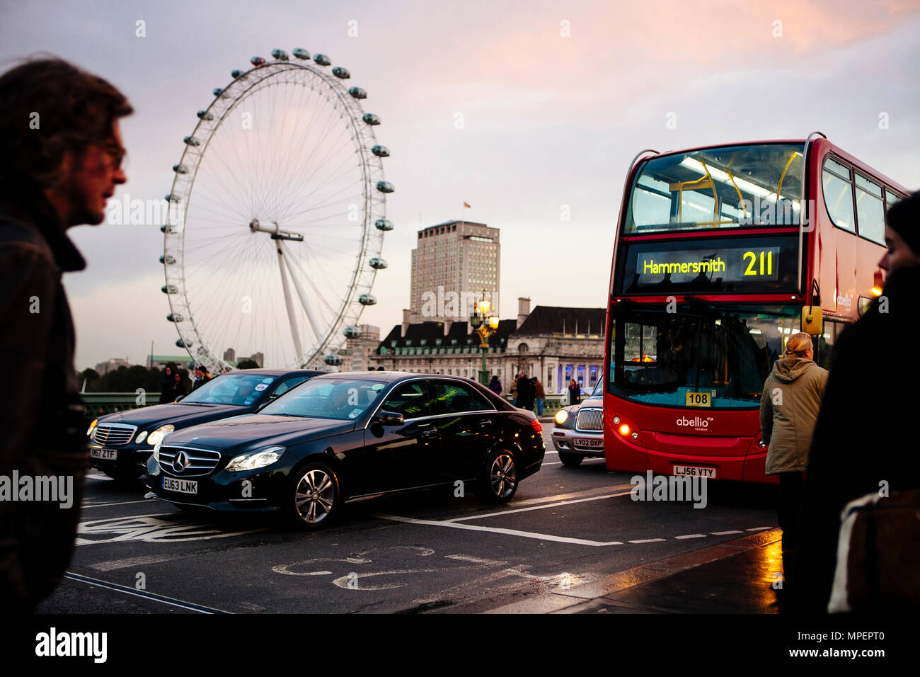 La gente in attesa per il traffico sul Westminster Bridge oltre il Tamigi con la London Eye o Millennium Wheel in prima serata. Foto Stock