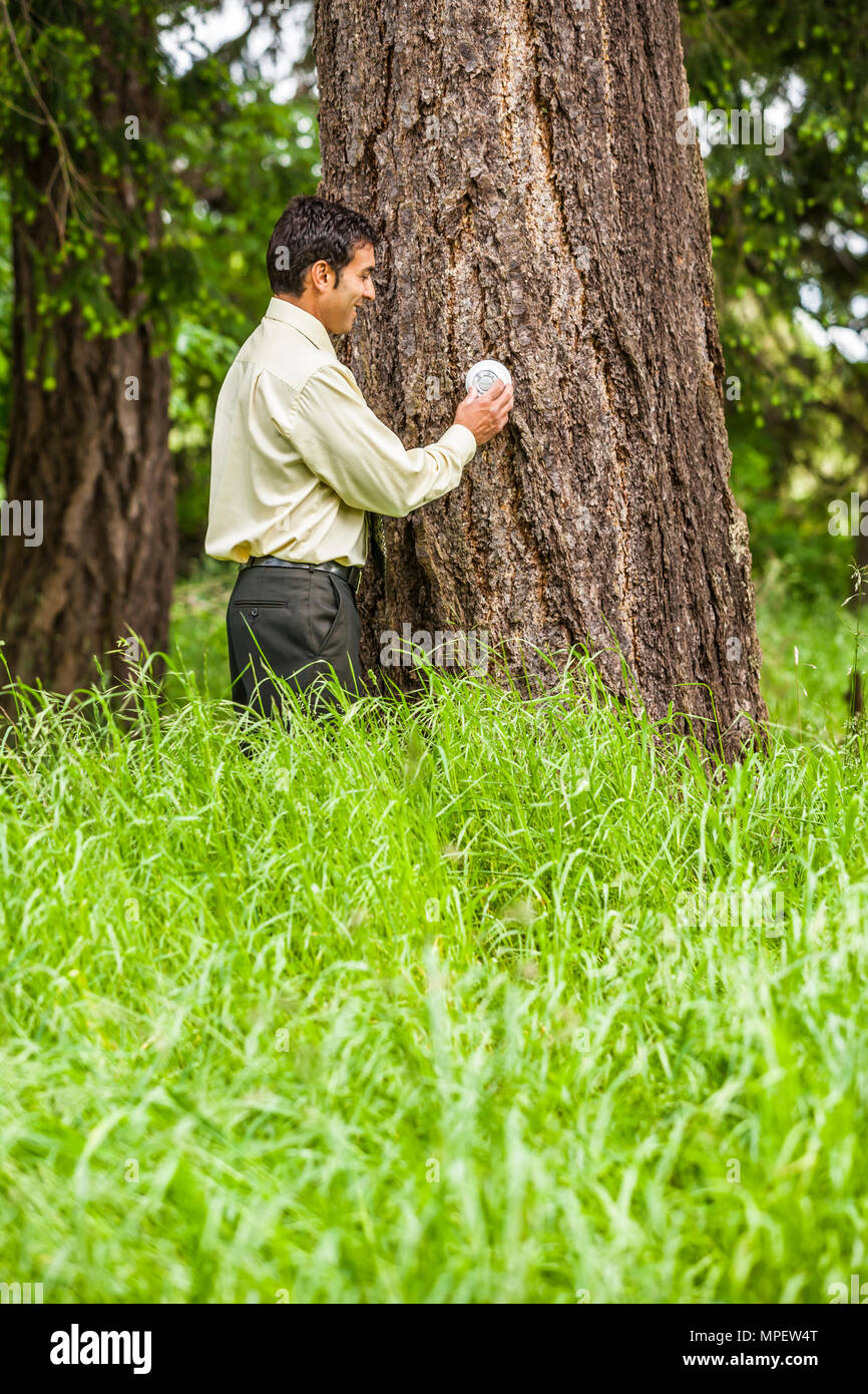 Inquadratura concettuale di un imprenditore di regolazione di un termostato attaccato all'albero accanto a lui. Illustrare il cambiamento climatico / Riscaldamento globale o ruotando verso il basso Foto Stock