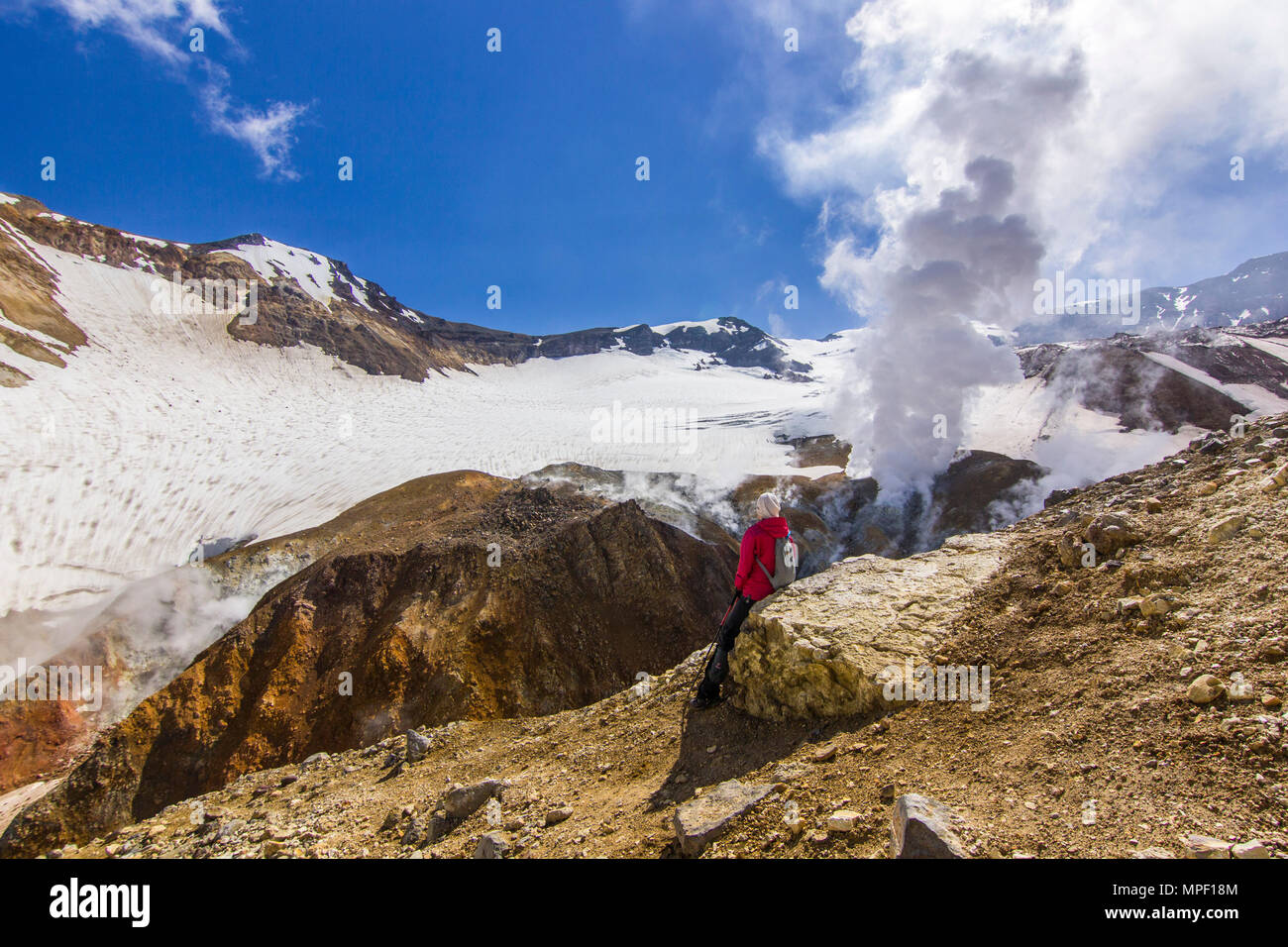 Ragazza seduta vicino al cratere fumante del vulcano attivo coperte da neve Foto Stock