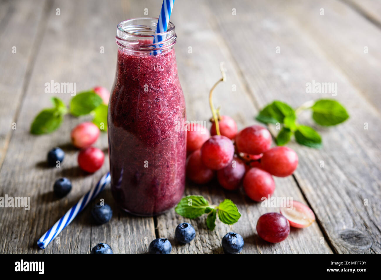 Fresca uva rossa e mirtillo frullati in una bottiglia di vetro Foto Stock