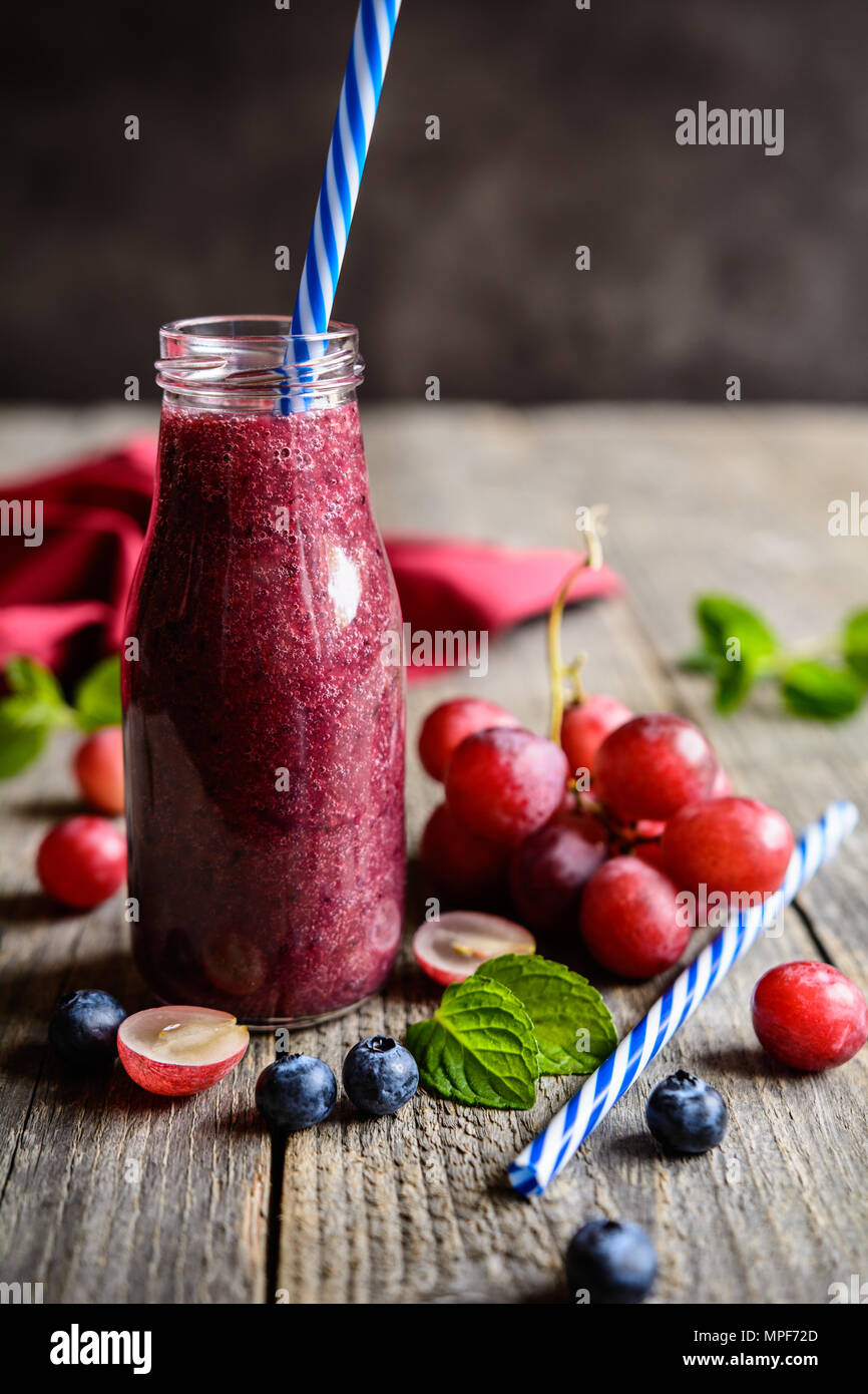 Fresca uva rossa e mirtillo frullati in una bottiglia di vetro Foto Stock