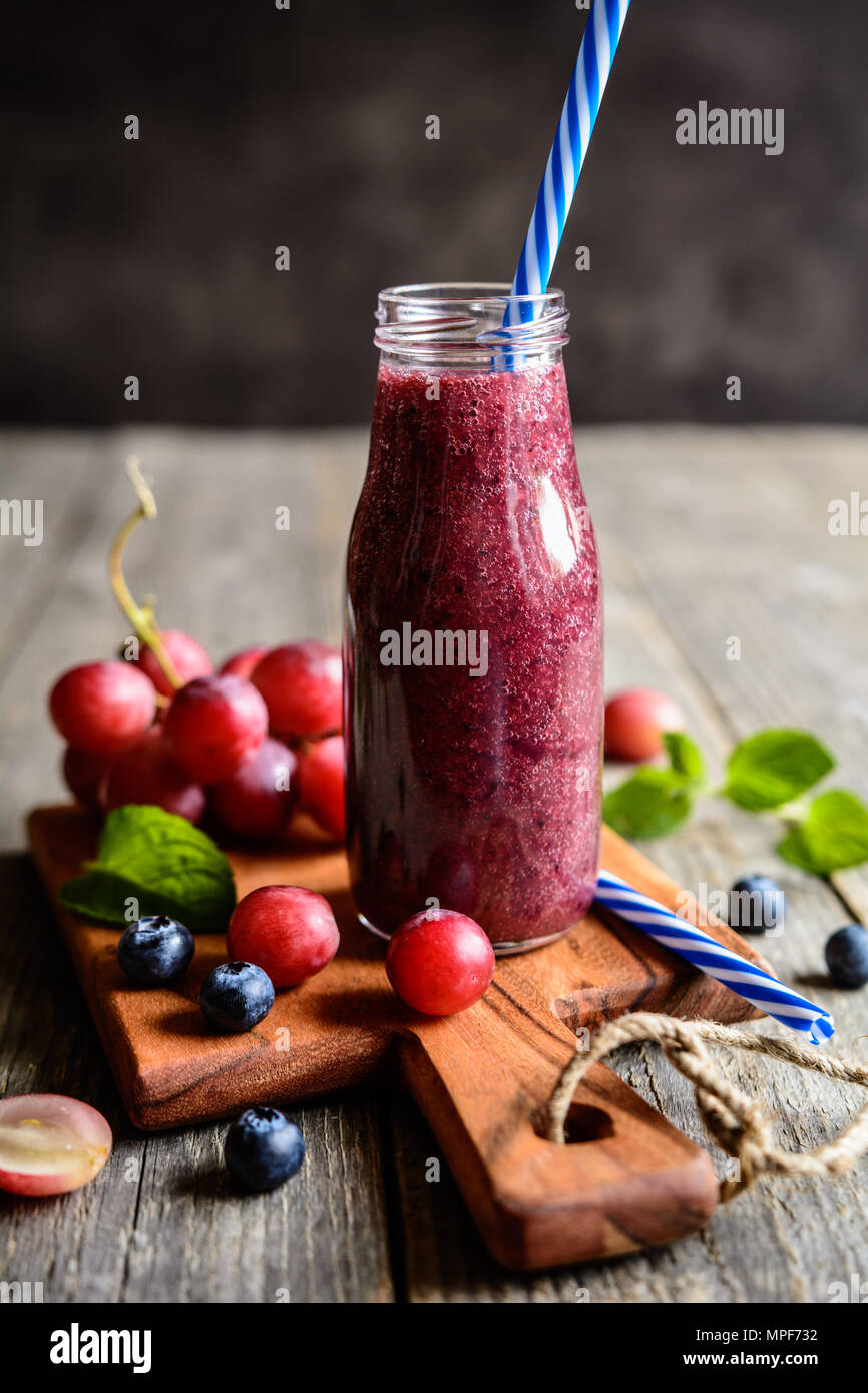 Fresca uva rossa e mirtillo frullati in una bottiglia di vetro Foto Stock
