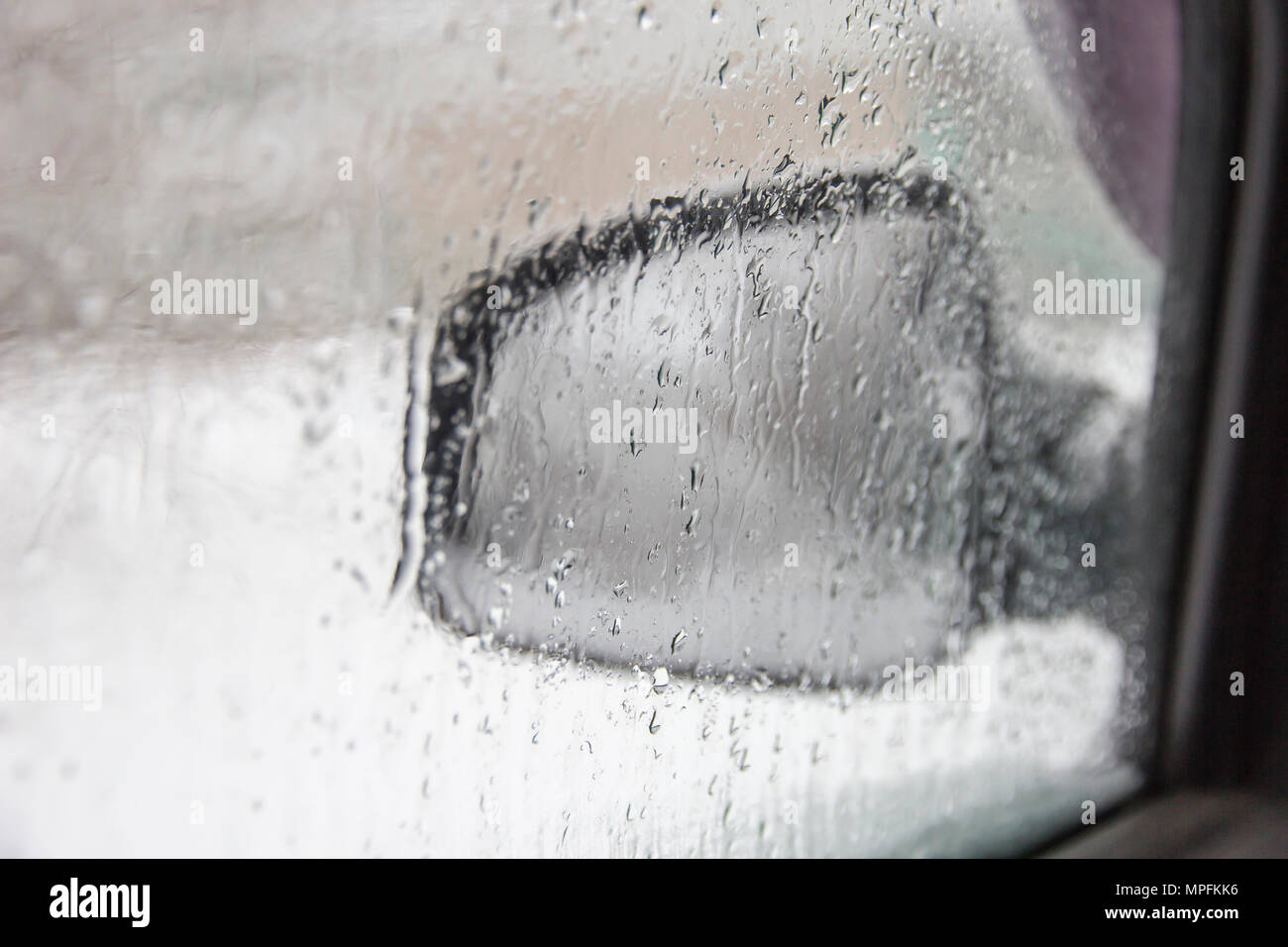 Auto laterale specchietto retrovisore attraverso la finestra sfuocata con gocce di pioggia Foto Stock