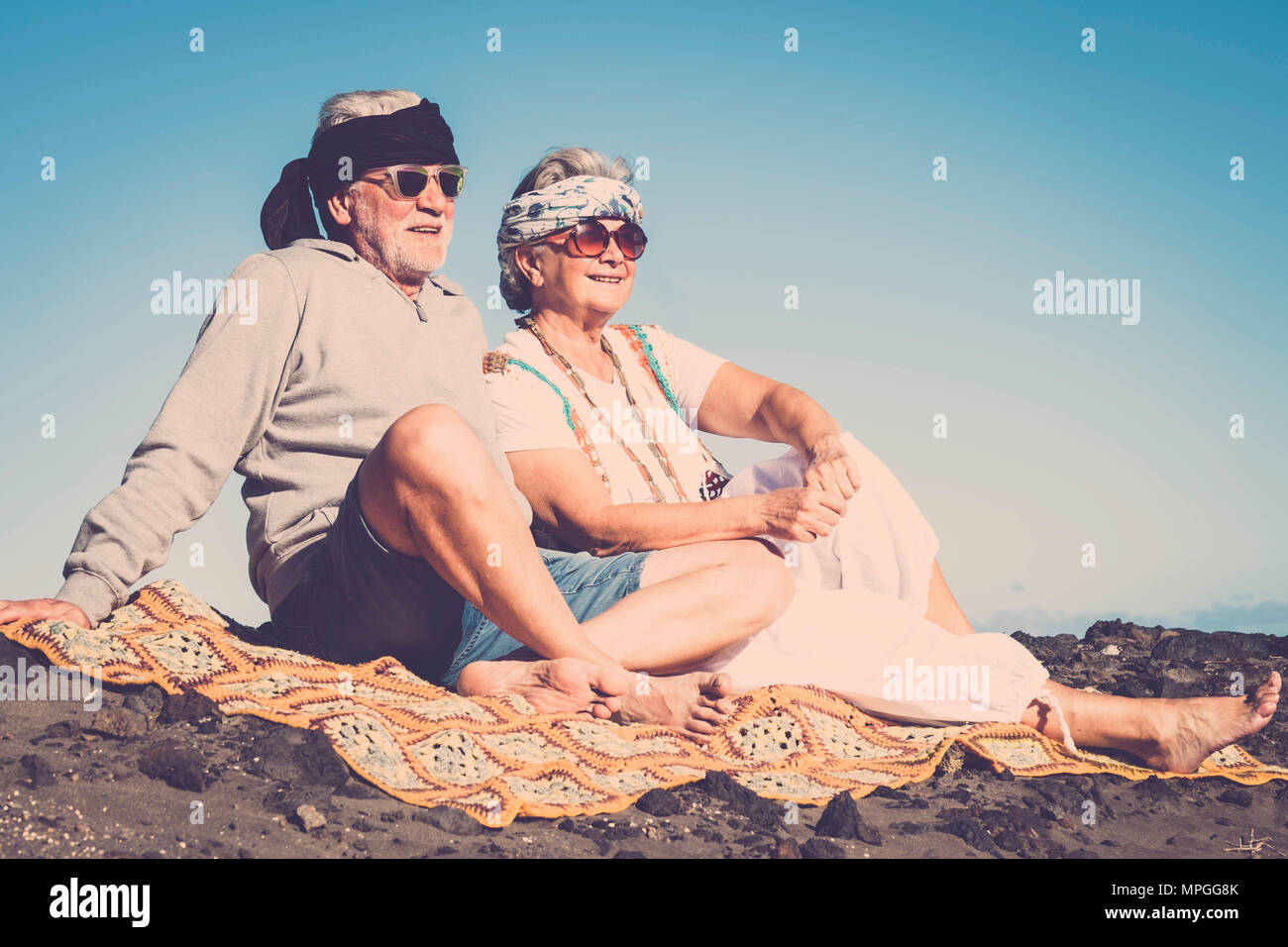 Paio di senior caucasica stile hippy e vita resto sulla spiaggia rocciosa a Tenerife. i colori e lo stile di vita alternativo per totalmente il concetto di libertà nelle vicinanze Foto Stock
