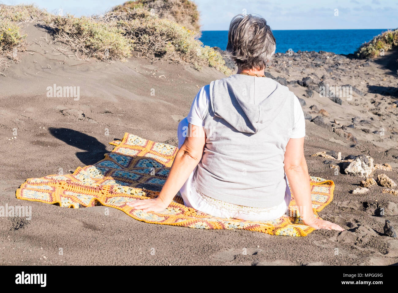 I capelli bianchi vecchia donna senior di sedersi e resto vicino all'oceano. outdoor e luogo naturale con il blu del cielo e acqua Foto Stock