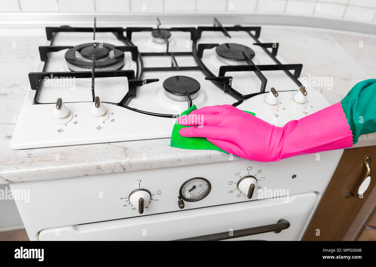 Mano nei guanti di gomma pulisce una cucina stufa a gas. Foto Stock