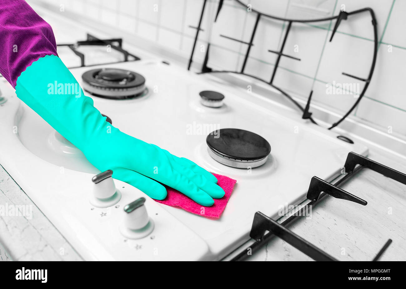 Mano nei guanti di gomma pulisce una cucina stufa a gas. Foto Stock