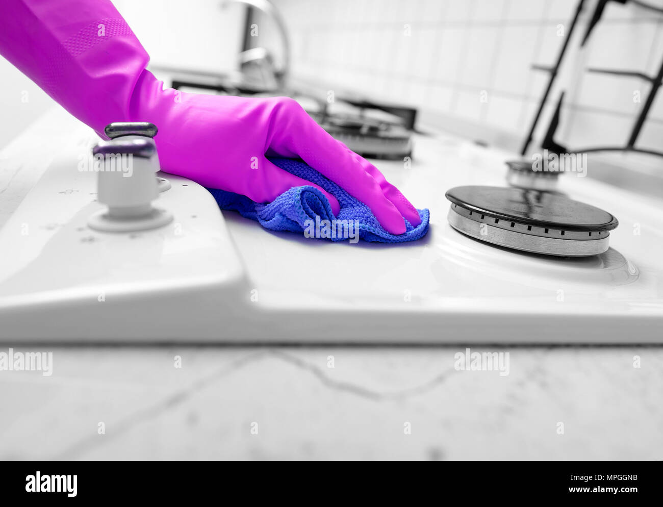 Mano nei guanti di gomma pulisce una cucina stufa a gas. Foto Stock