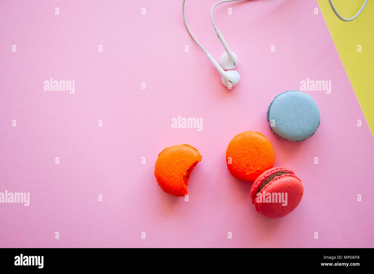 Francese colorati macaron cookie e cuffie su una rosa e sfondo giallo. Relax, lo stile di vita del concetto. Vista superiore e spazio di copia. Foto Stock