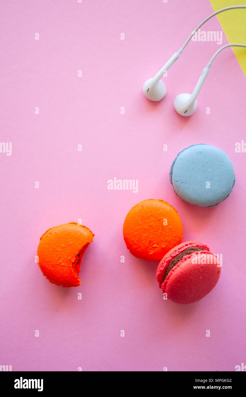 Francese colorati macaron cookie e cuffie su una rosa e sfondo giallo. Relax, lo stile di vita del concetto. Vista superiore e spazio di copia. Foto Stock