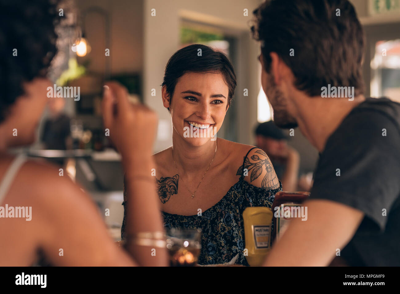 Bella giovane donna sorridente e parlando con i suoi amici in un caffè. Un gruppo di giovani riuniti presso il ristorante. Foto Stock