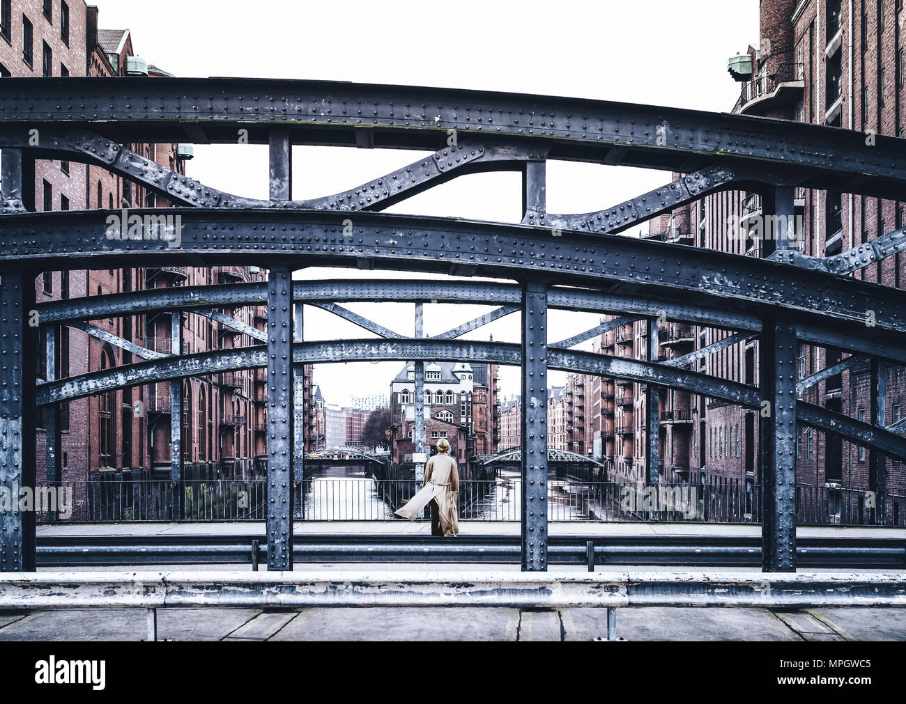 Vista posteriore della donna che indossa lungo cappotto in piedi sul ponte vecchio in warehouse district Speicherstadt di Amburgo Foto Stock