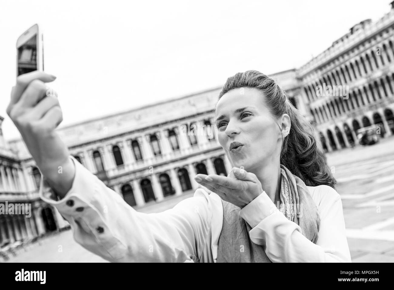 Giovane donna bacio di soffiaggio e rendendo selfie su piazza san marco a venezia, Italia Foto Stock